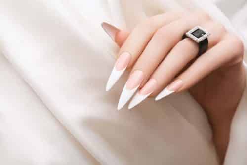 Female hand with french stiletto nail design. Long pink nail polish manicure. Woman hand on white fabric background.