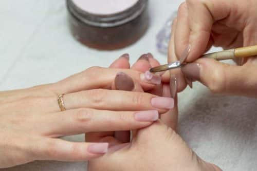 applying a brush on acrylic nails in the salon