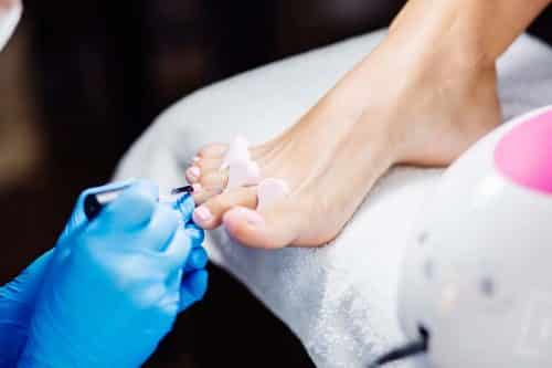 gel pedicure. Foot care treatment and nail. The process of professional pedicures. Master in blue gloves apply light pink gel polish.